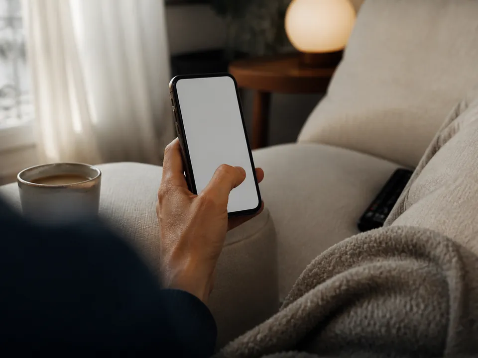 Main tenant un smartphone affichant un écran flou, café à côté